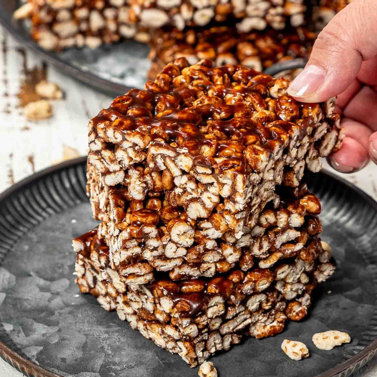 3 pieces of puffed wheat squares on a plate with a hand holding the top one.