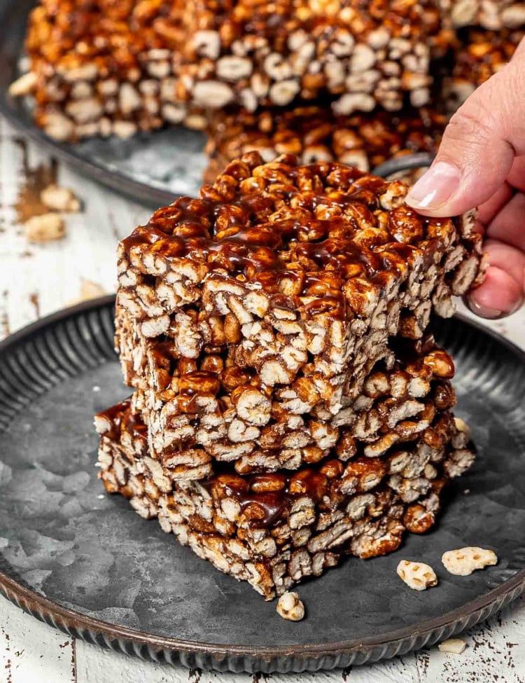 3 pieces of puffed wheat squares on a plate with a hand holding the top one.