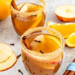 two glasses with homemade apple cider garnished with a cinnamon stick and a few apple slices.