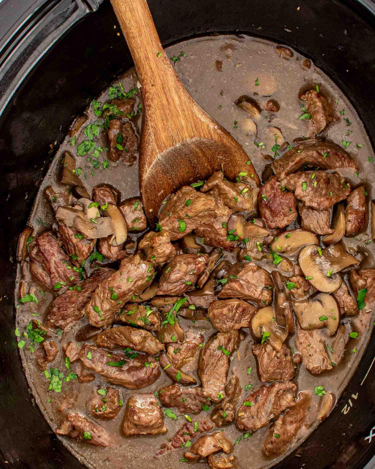 a crockpot with steak and gravy garnished with parsley.