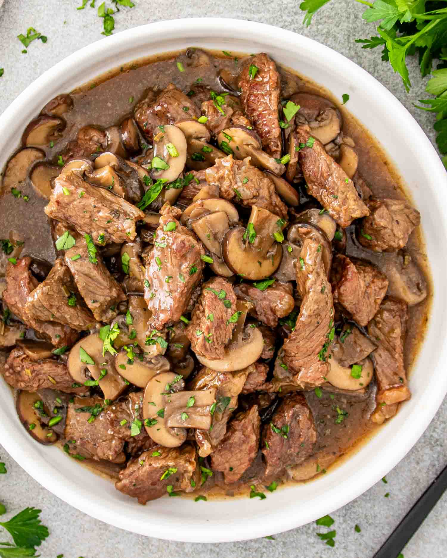 a white bowl full of steak and gravy made in a crockpot garnished with parsley.
