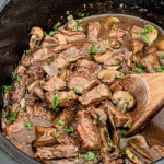a crockpot with steak and gravy garnished with parsley.