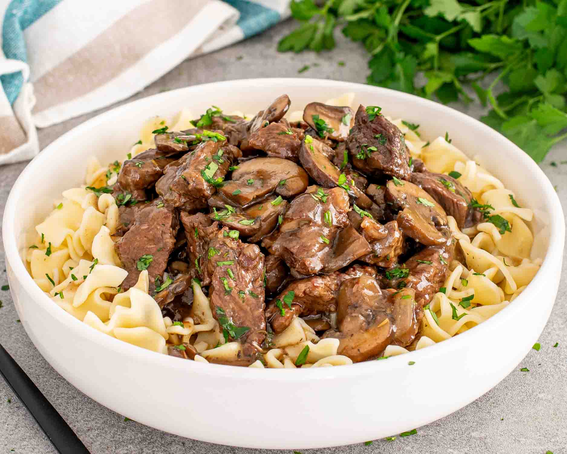 a white bowl with noodles topped with steak and gravy made in the crockpot.