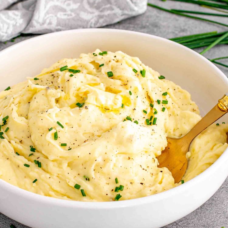 a white bowl with garlic mashed potatoes and a pat of butter on top and garnished with chives.
