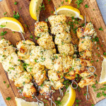 garlic parmesan chicken skewers on a cutting board garnished with lemon wedges.
