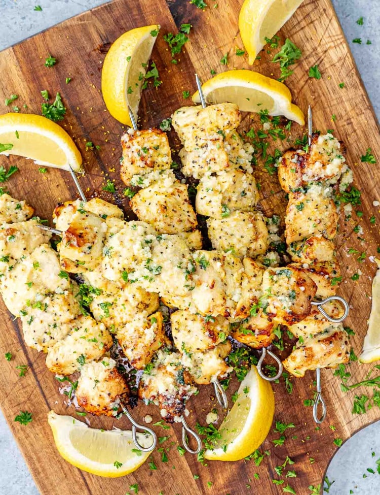 garlic parmesan chicken skewers on a cutting board garnished with lemon wedges.