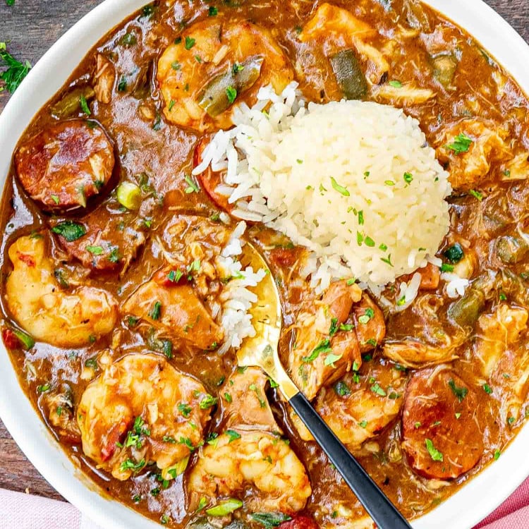 freshly made gumbo in a white bowl with a scoop of rice and garnished with some parsley.