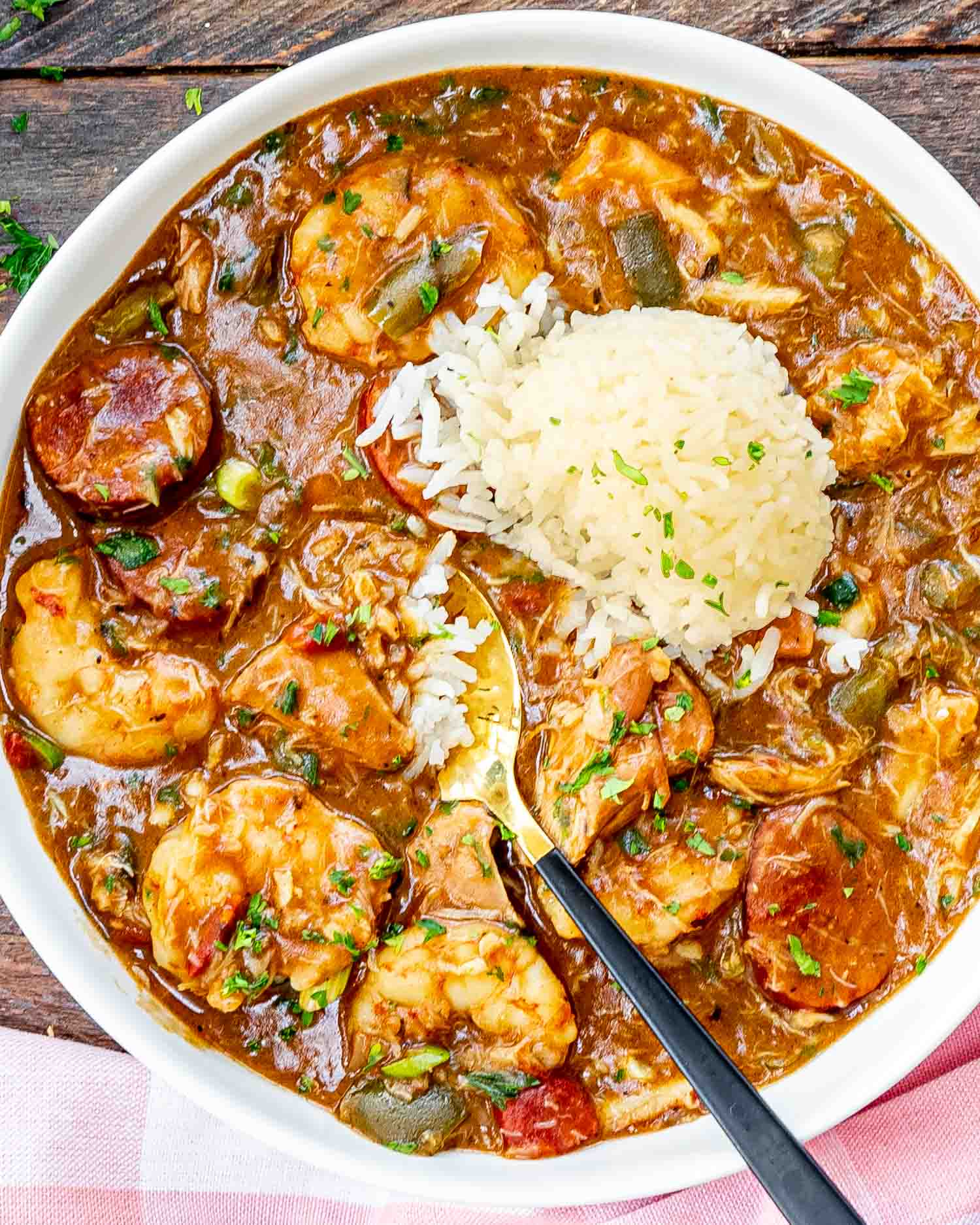 freshly made gumbo in a white bowl with a scoop of rice and garnished with some parsley.
