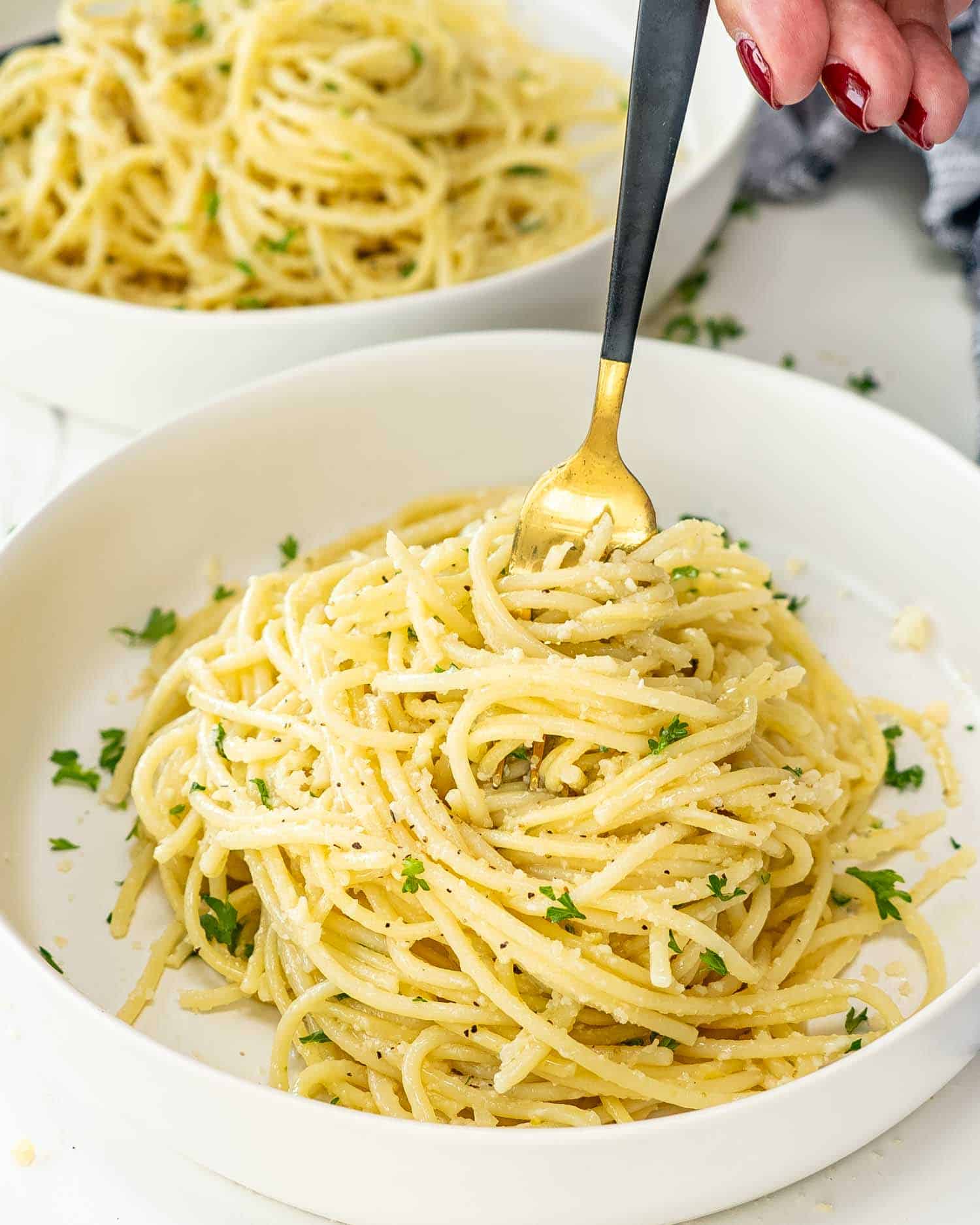 a serving of lemon pasta in a white bowl garnished with parsley and parmesan cheese.