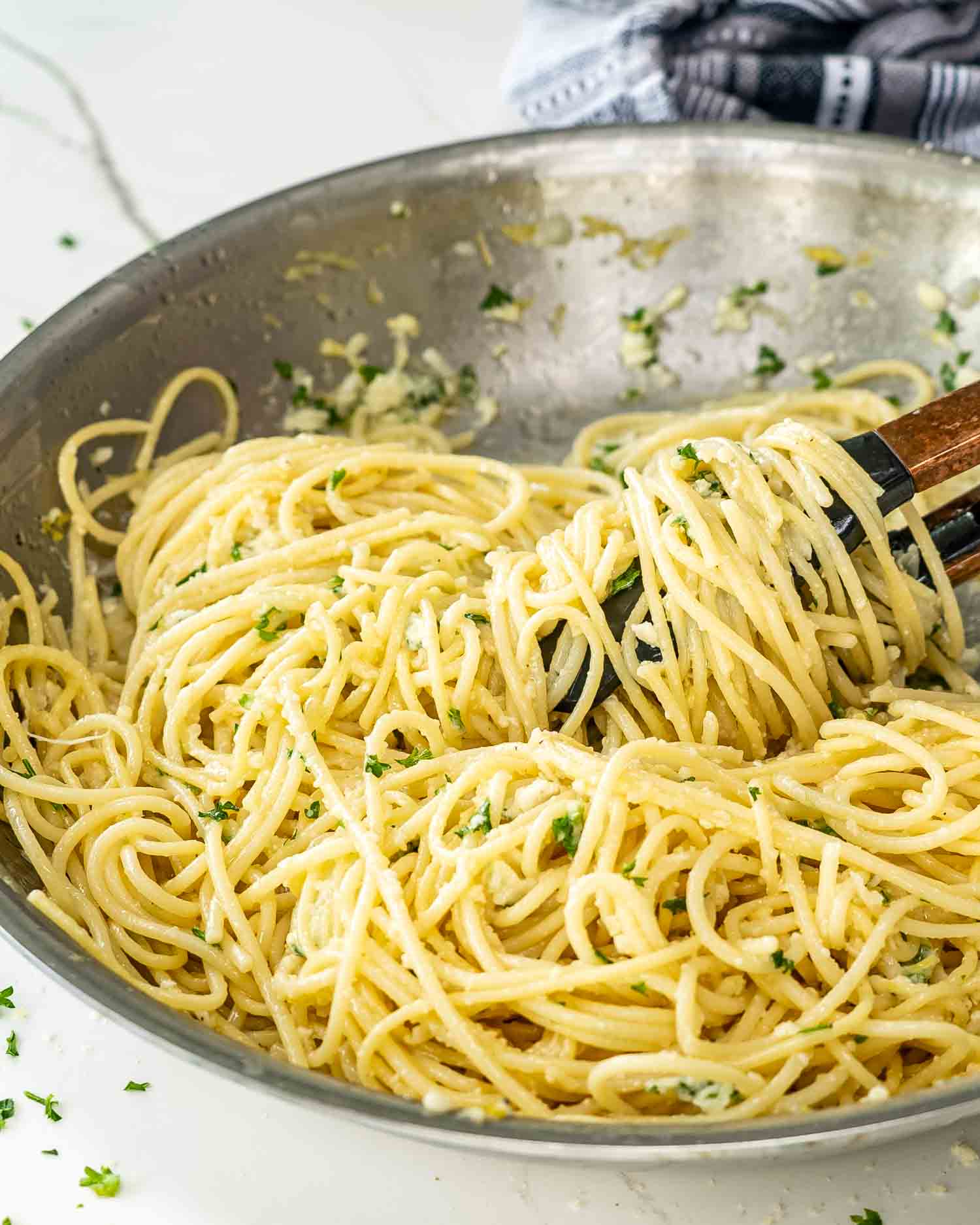 a skillet with lemon pasta in it with a pair of tongs twirling some pasta.