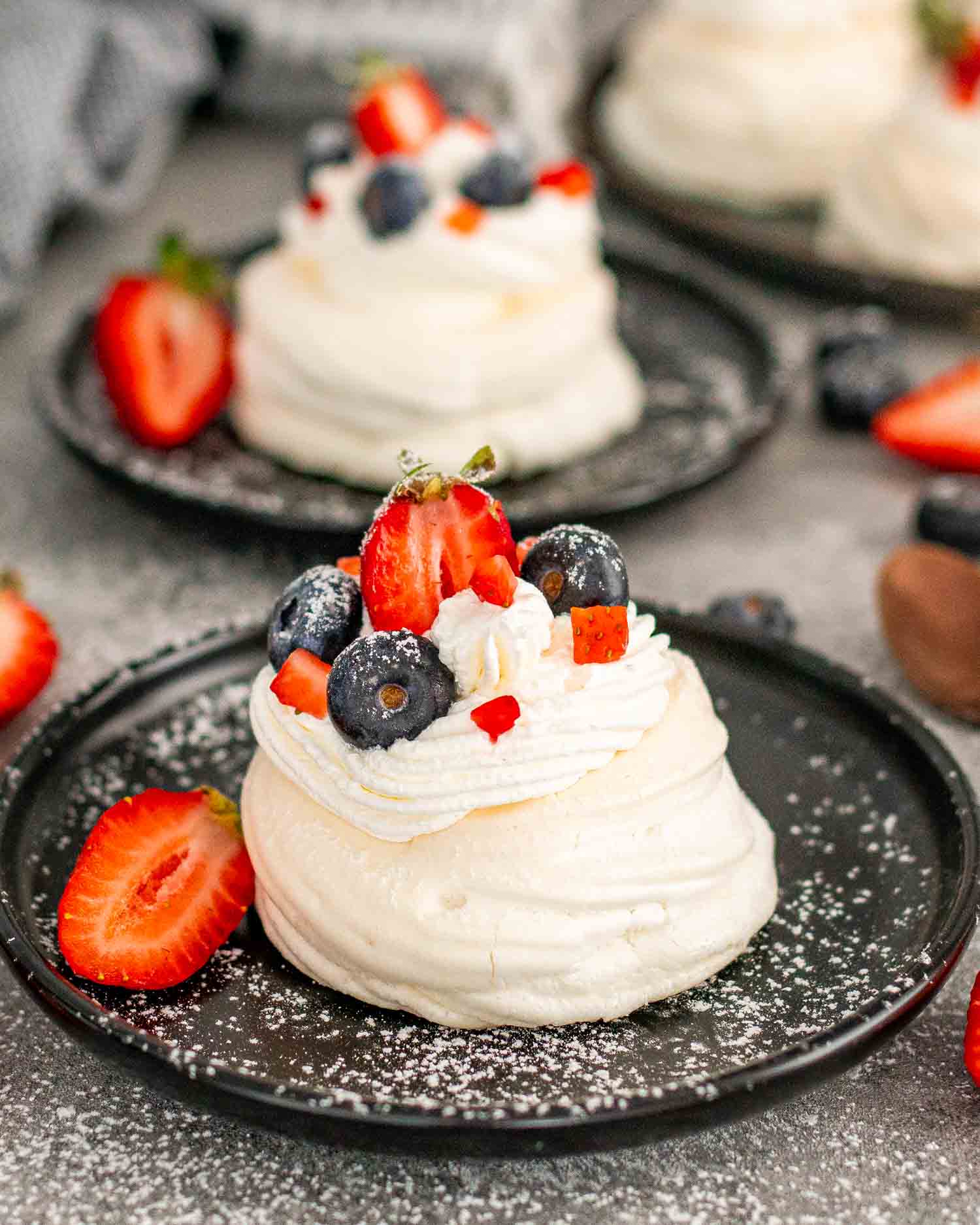 mini pavlova on a metal plate topped with whipped cream and berries.