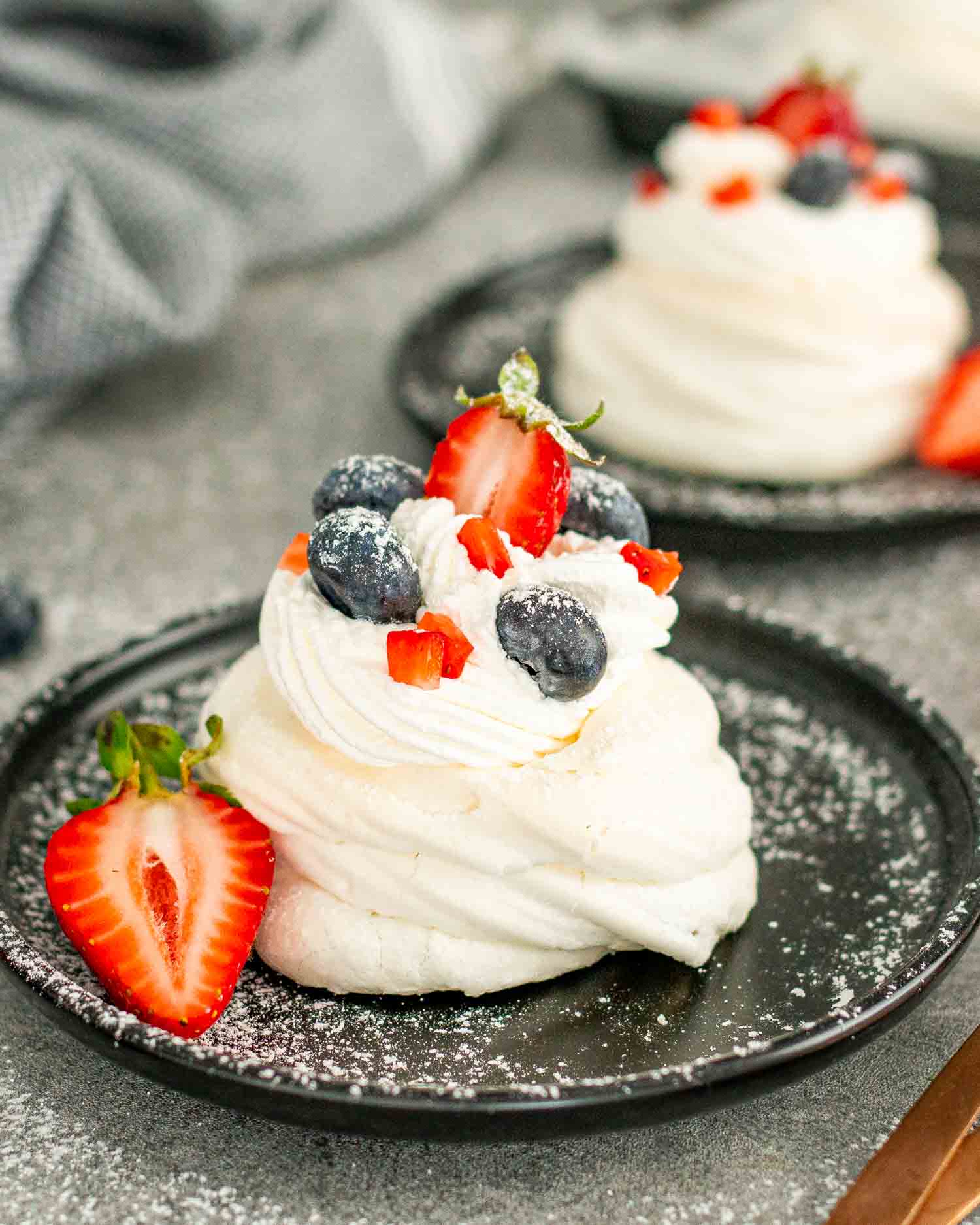 mini pavlova on a metal plate topped with whipped cream and berries.