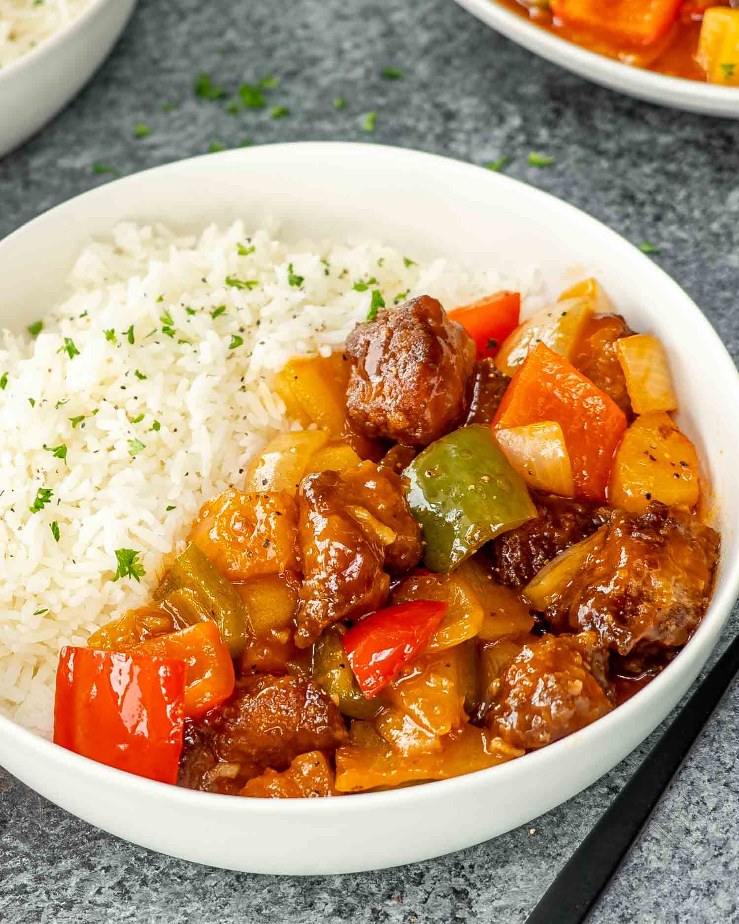 sweet and sour pork on a bed of rice in a white bowl.