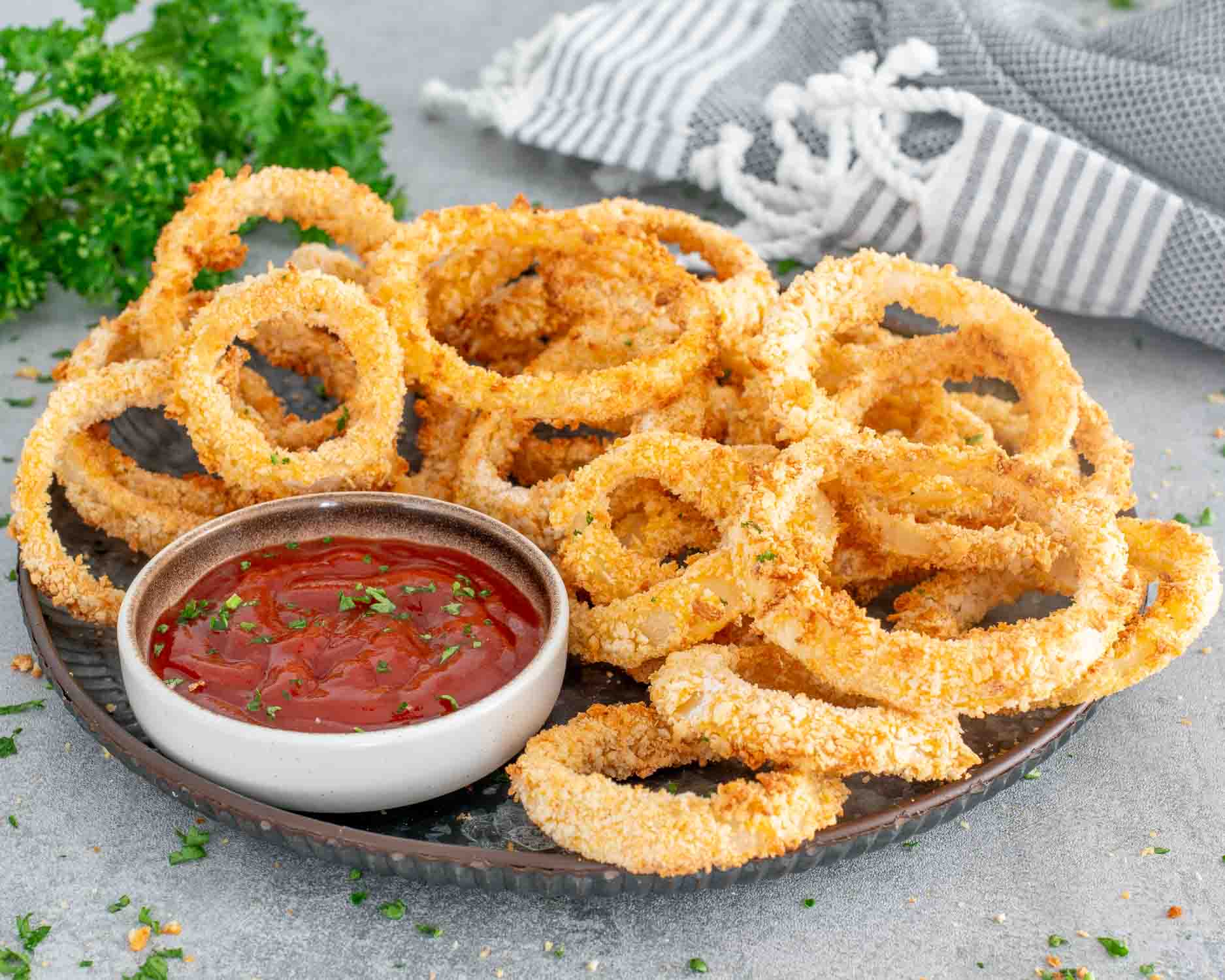 freshly made onion rings in the air fryer on a metal plate with ketchup.