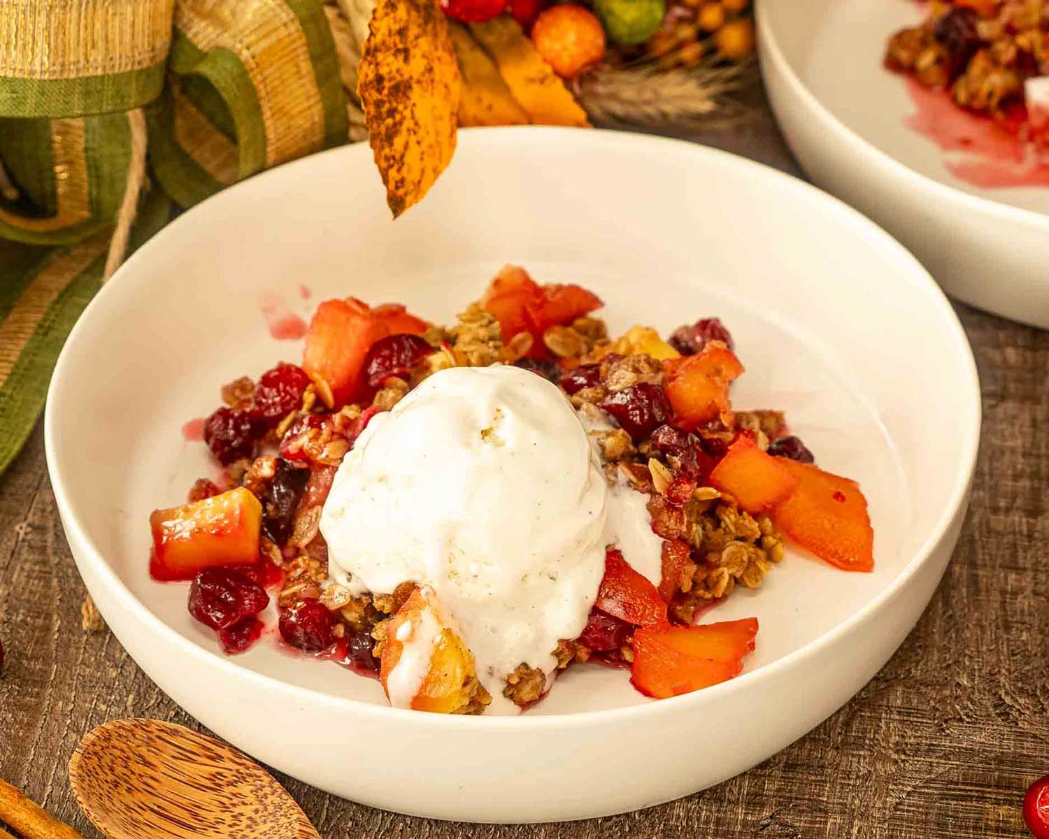 a serving of apple cranberry crisp with a dollop of vanilla ice cream in a white bowl.