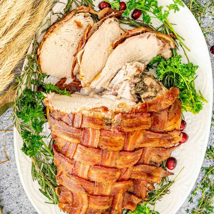 bacon wrapped turkey breast sliced on a turkey platter.