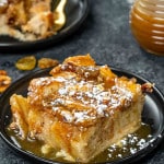 a slice of bread pudding with caramel sauce on a black plate.