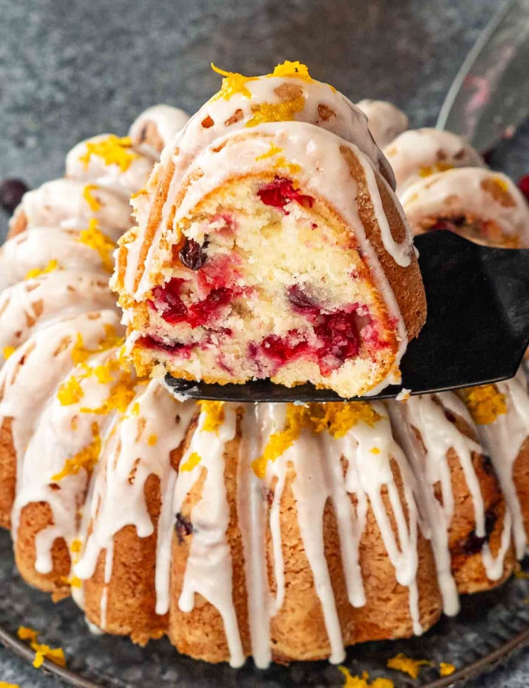 a delicious and gorgeous cranberry coffee cake on a serving plate glazed with a lemon glazed and garnished with orange zest.