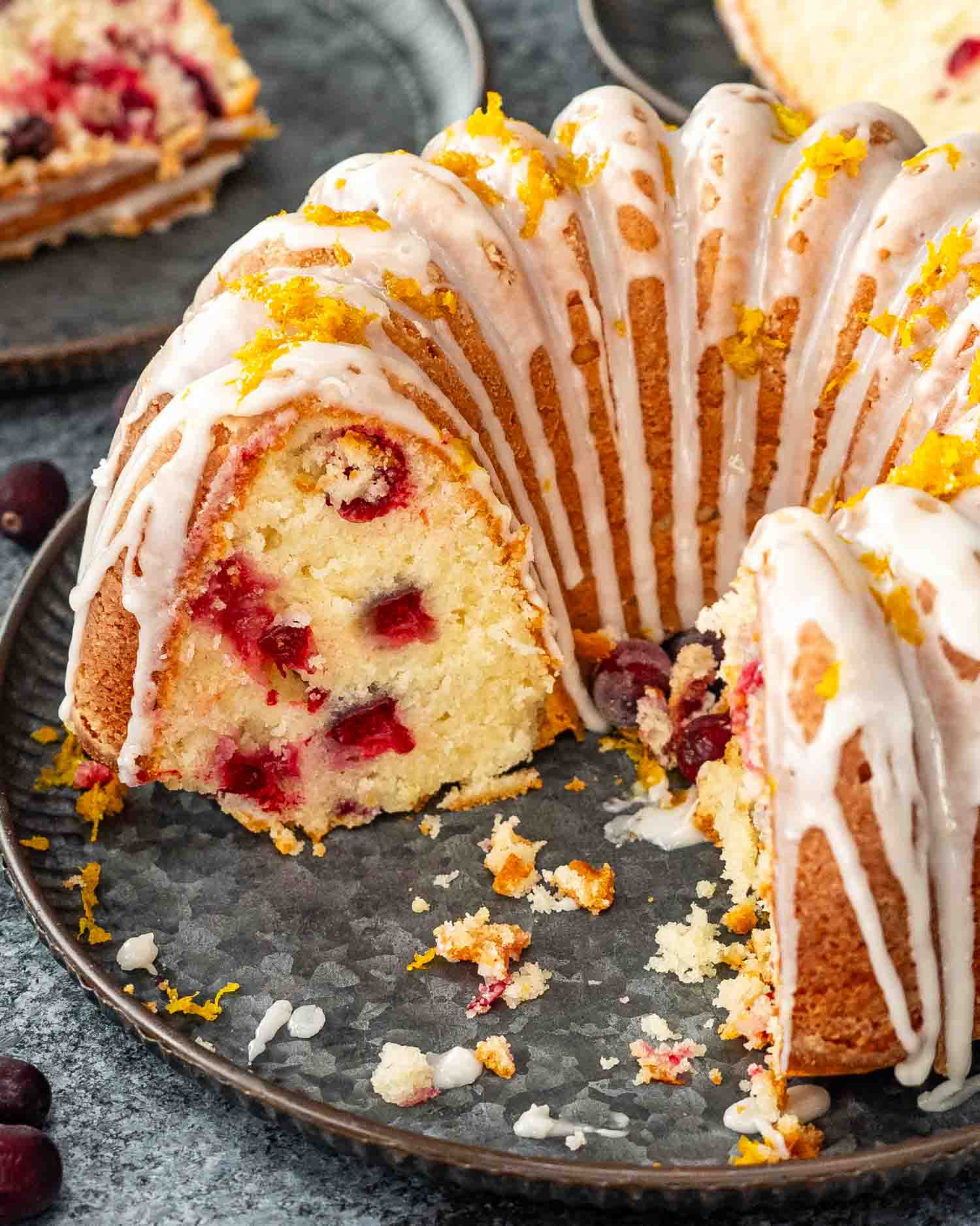 a delicious and gorgeous cranberry coffee cake on a serving plate glazed with a lemon glazed and garnished with orange zest.
