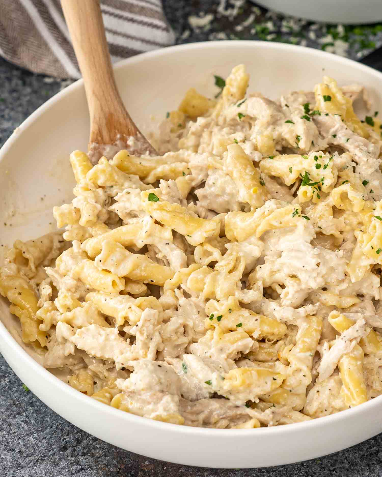 freshly made chicken alfredo in a crockpot, in a large serving bowl with a wooden spoon inside.
