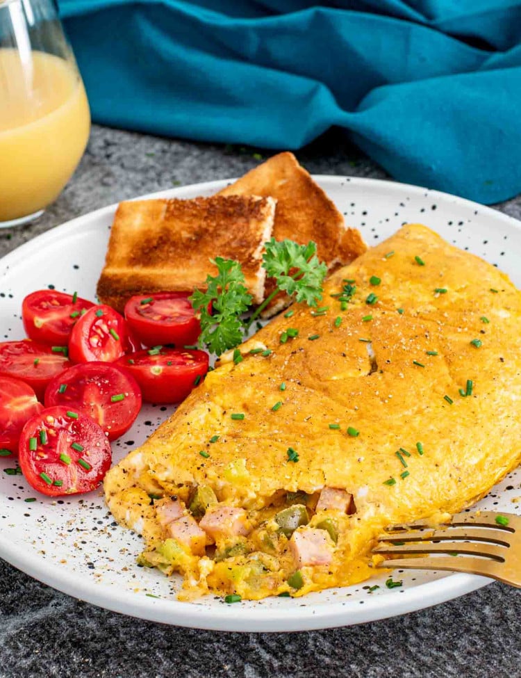a denver omlette on a plate alongside some cherry tomatoes and toast.