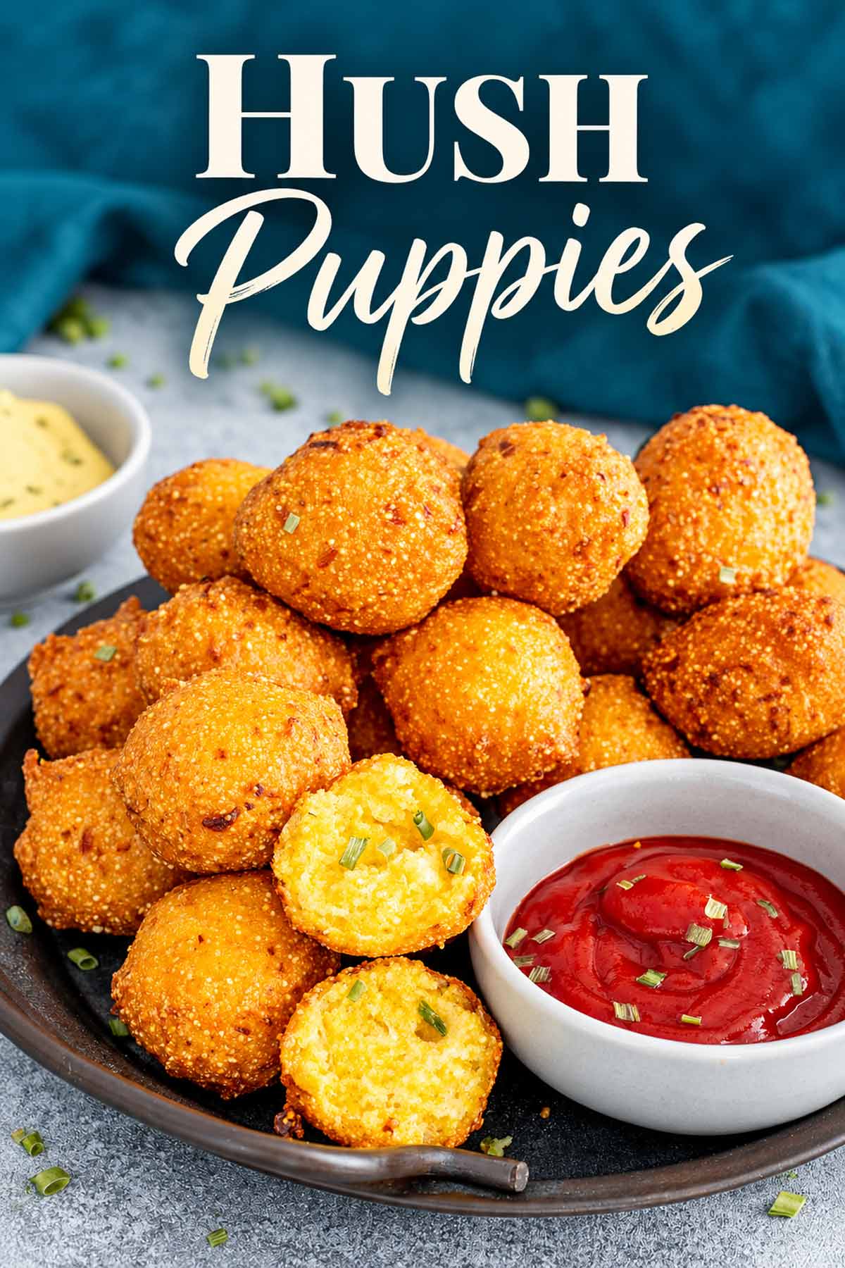 Golden homemade hush puppies piled on a platter with red dipping sauce and one cut open to show the center.