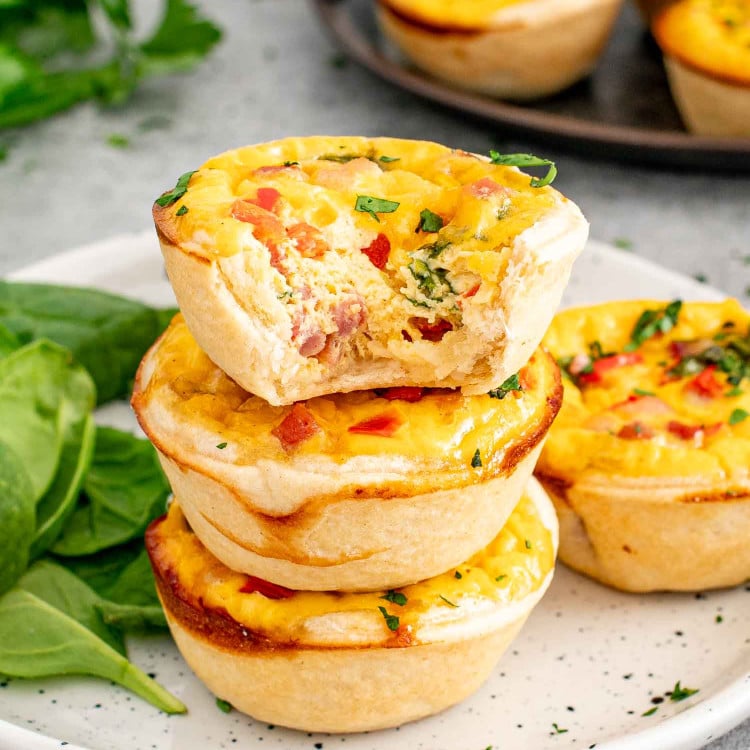 a few mini quiches stacked on a plate with one having a bite taken out of it.