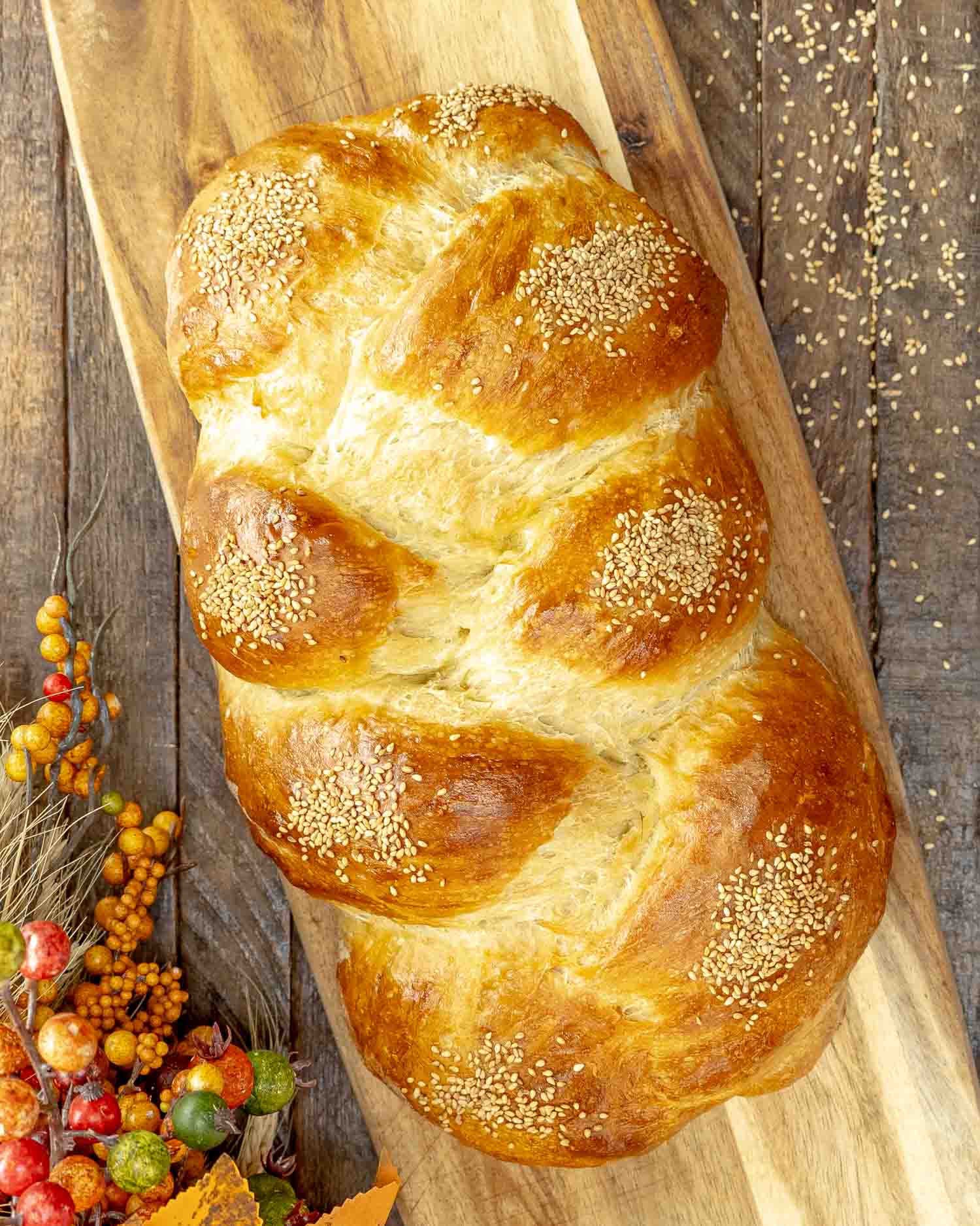 Golden-brown braided challah bread sprinkled with sesame seeds on a wooden paddle board.