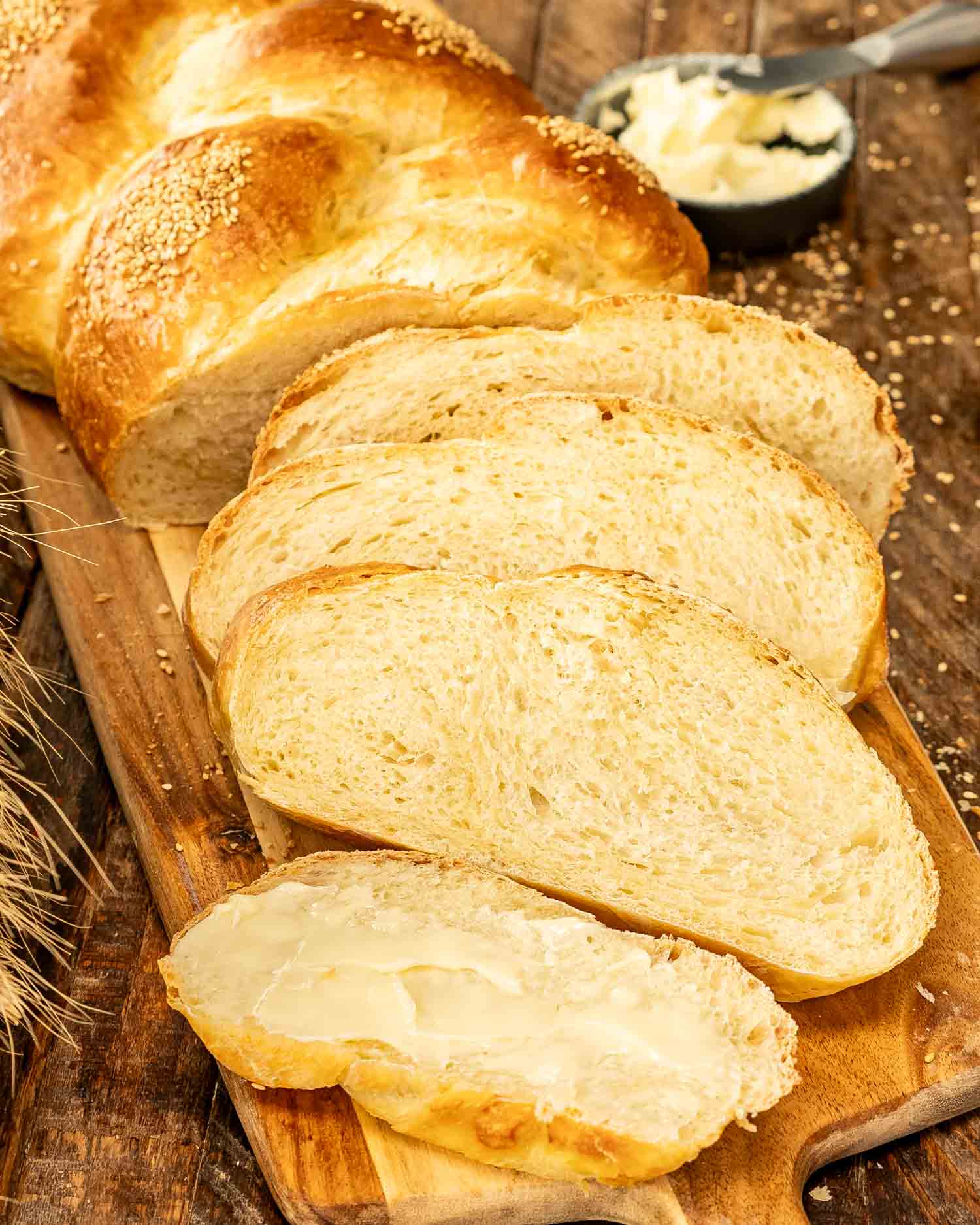 A fresh, golden-braided no knead challah bread on a wooden board with slices and butter nearby.