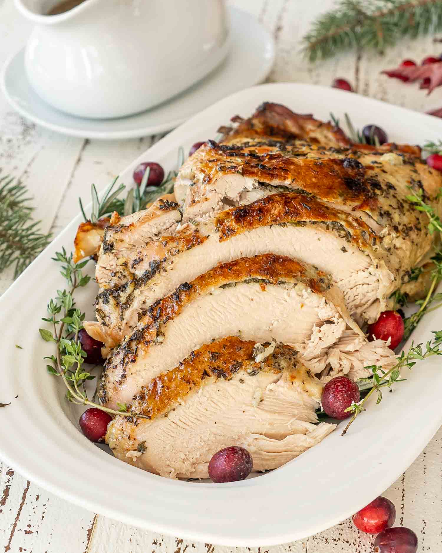 Herb-crusted carved slow cooker turkey breast on a platter with cranberries and a gravy boat in the back.