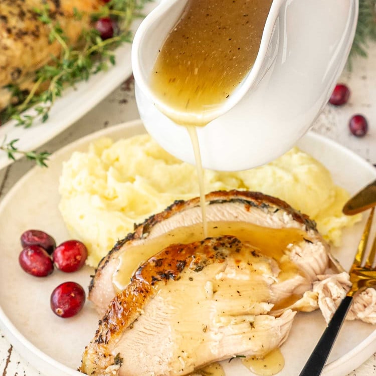 slow cooker turkey breast slices with gravy being poured over, served with mashed potatoes and cranberries.