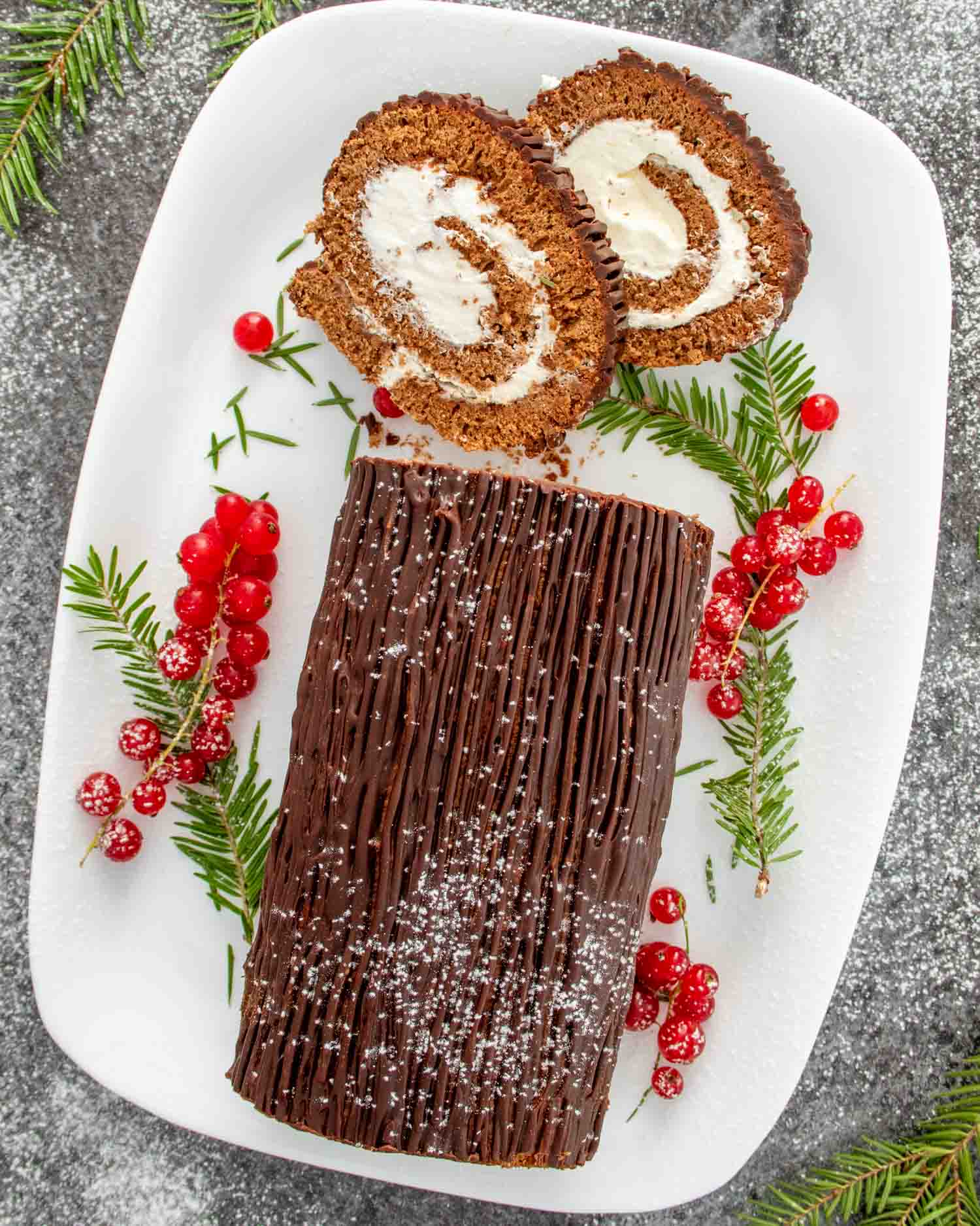 a buche de noel (yule log cake) on a white cake platter, with two slices cut out.