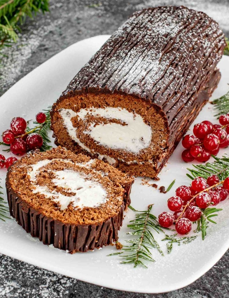 a buche de noel (yule log cake) on a white cake platter, with one slice cut out.