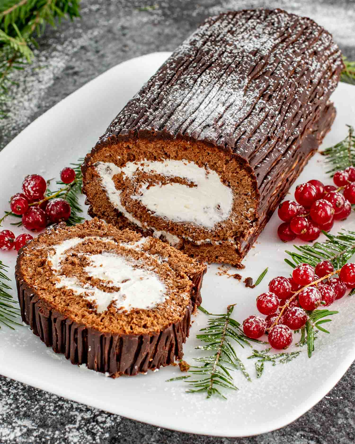 a buche de noel (yule log cake) on a white cake platter, with one slice cut out.