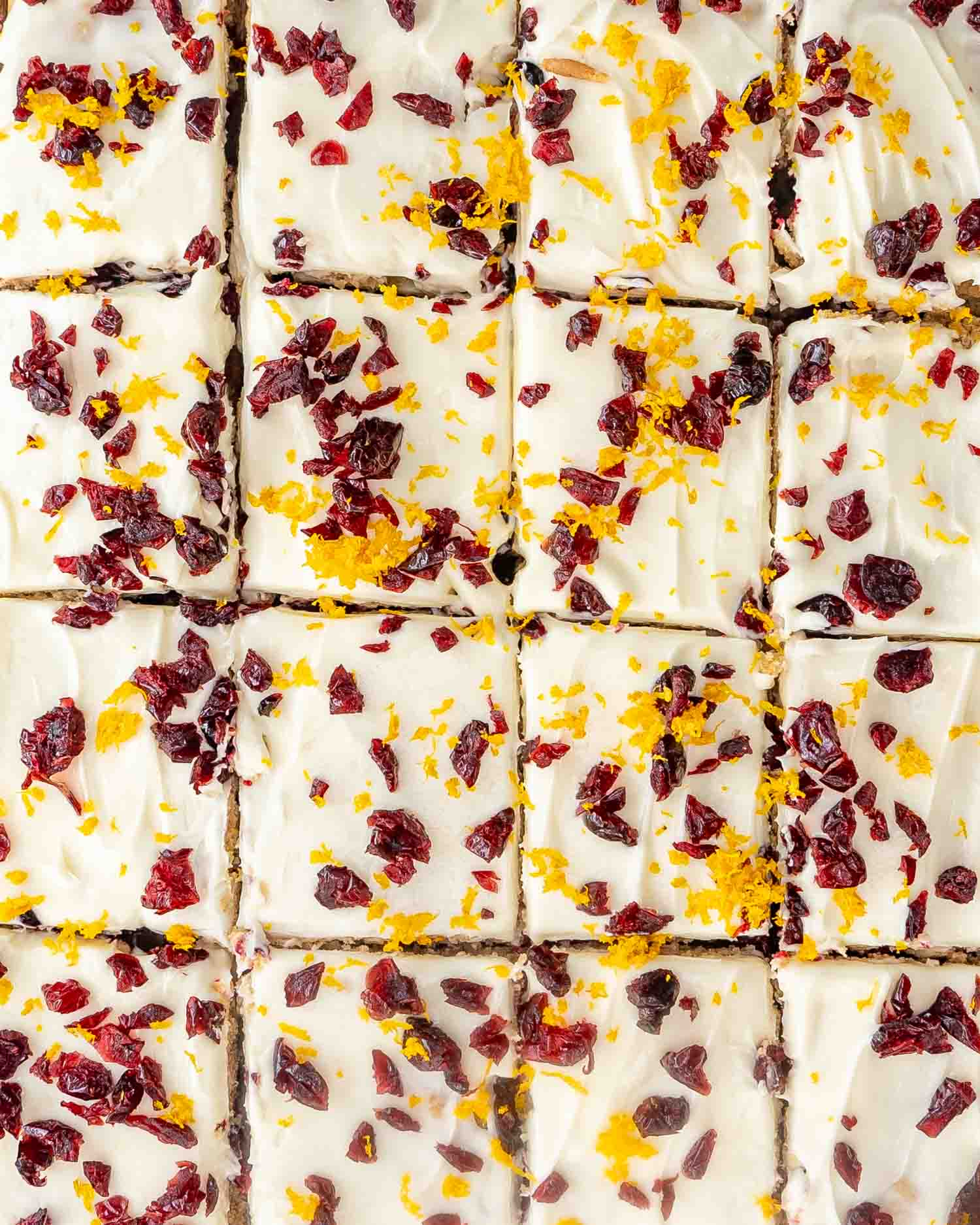 cranberry bars on a cutting board cut into squares and topped with dried cranberries and orange zest.