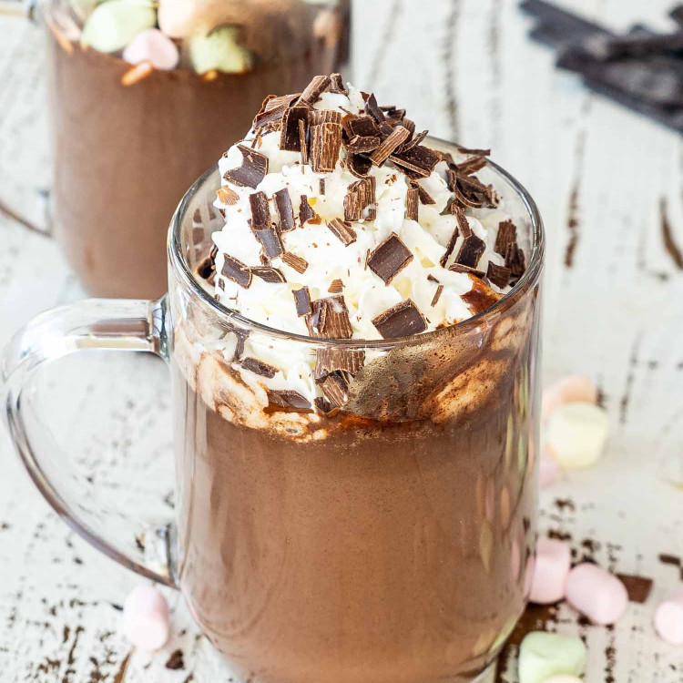 a hot chocolate in a mug topped with whipped cream and chocolate shavings.