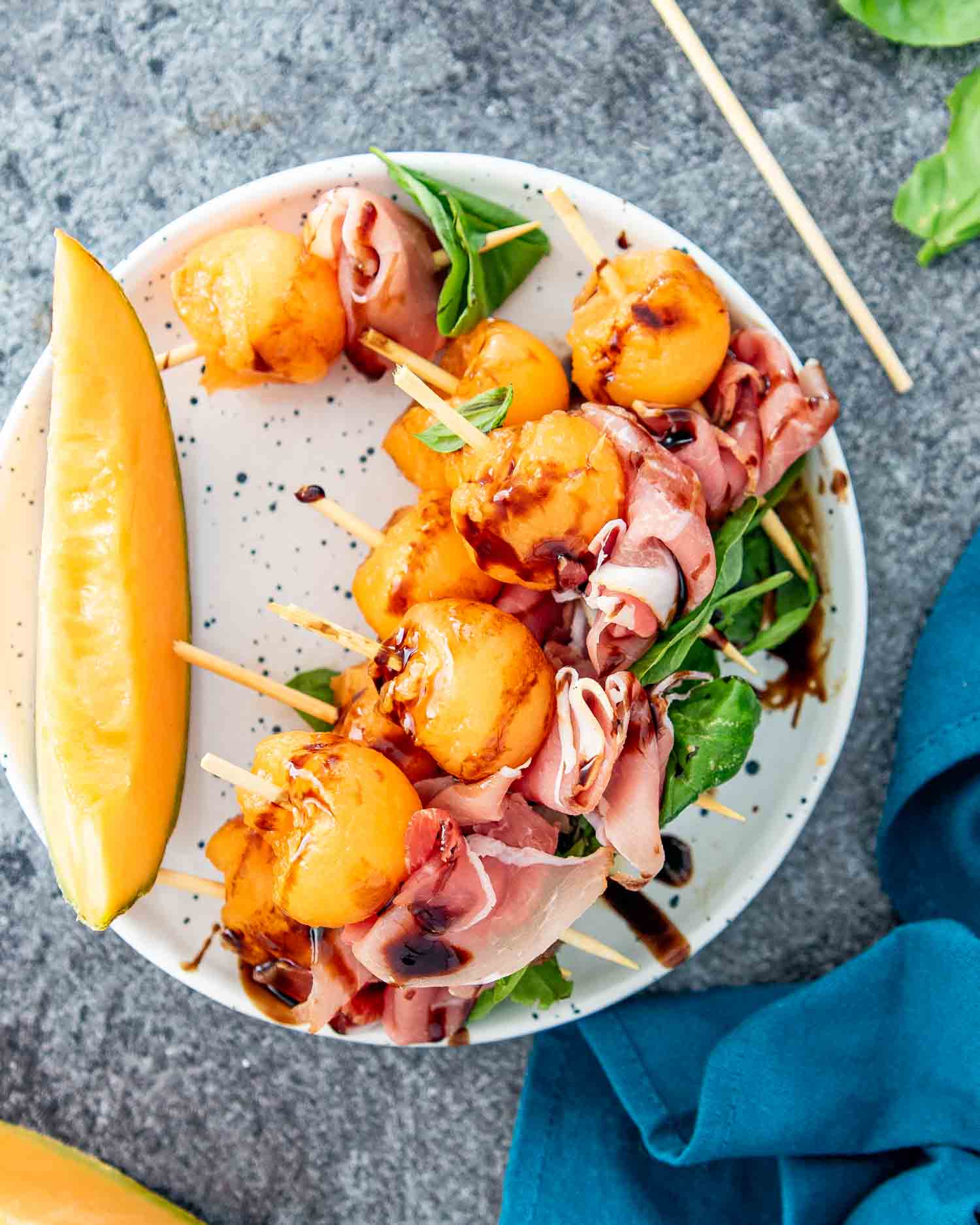 melon prosciutto skewers with balsamic glaze on a white plate.