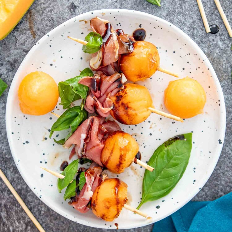 melon prosciutto skewers with balsamic glaze on a white plate.