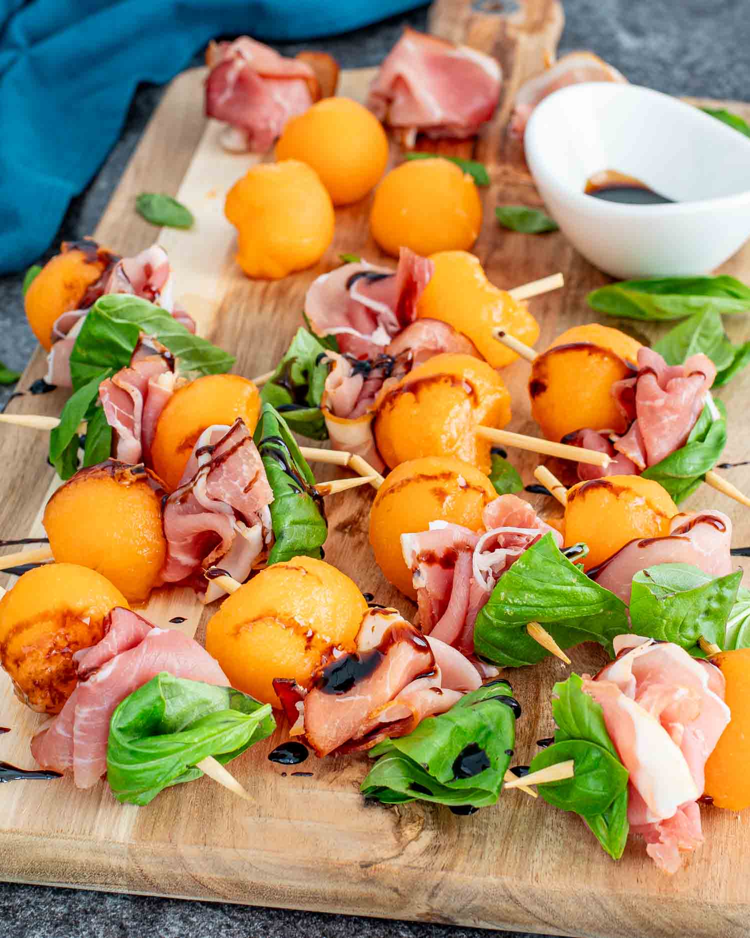 melon prosciutto skewers with balsamic glaze on a cutting board.