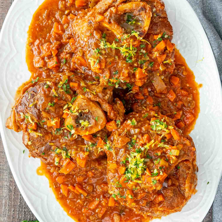 osso buco with gremolata and sauce on a white serving platter.