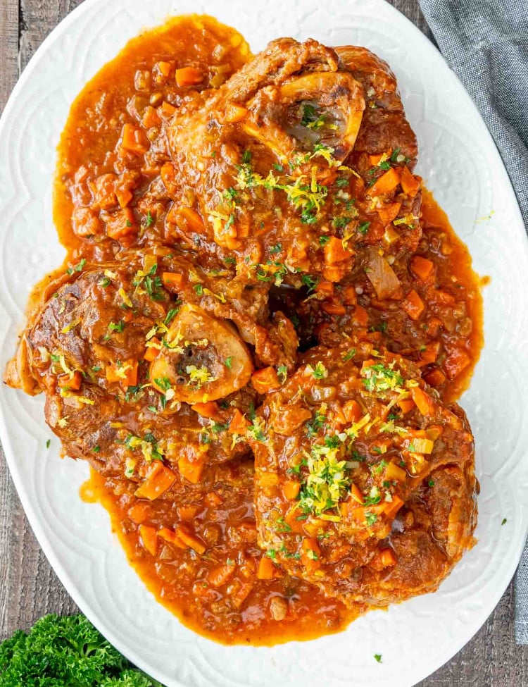 osso buco with gremolata and sauce on a white serving platter.