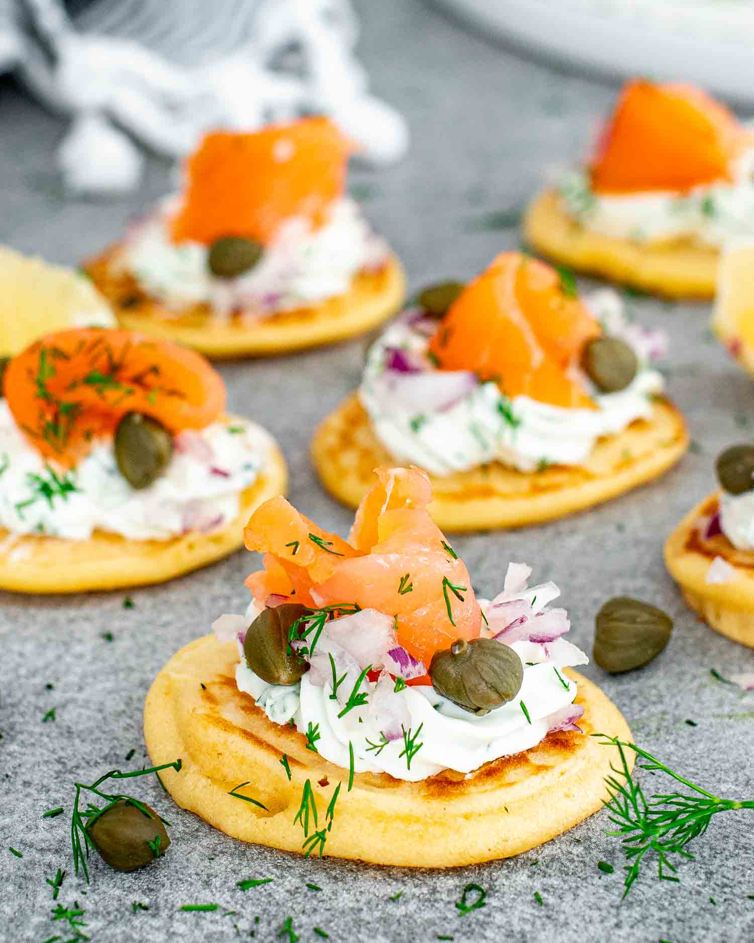 freshly made smoked salmon blinis on a gray plate garnished with lemon wedges.