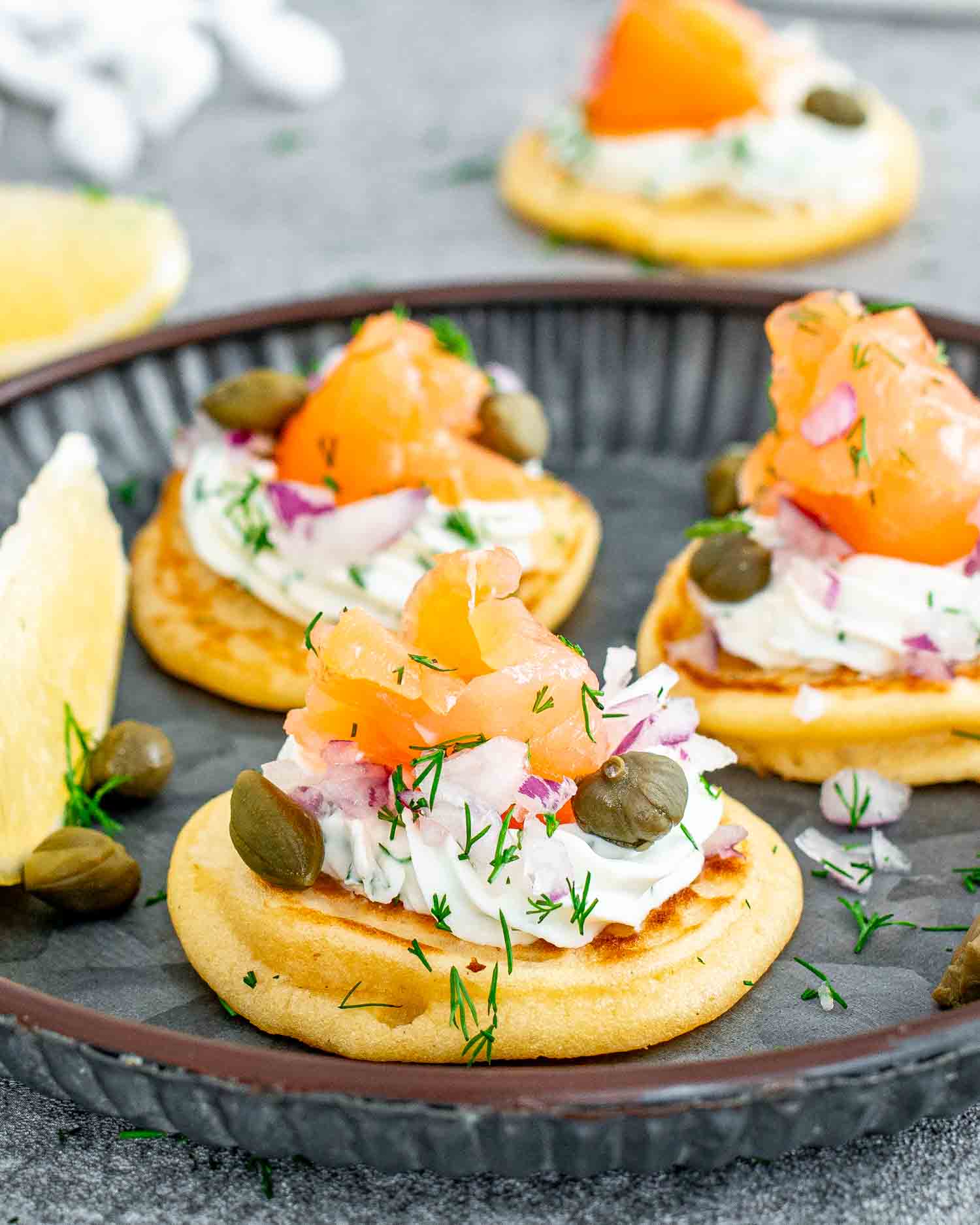 freshly made smoked salmon blinis on a gray plate garnished with lemon wedges.