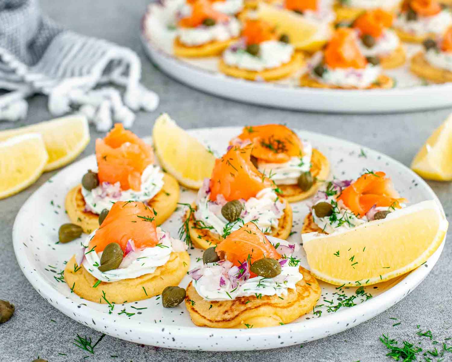 freshly made smoked salmon blinis on a white plate garnished with lemon wedges.