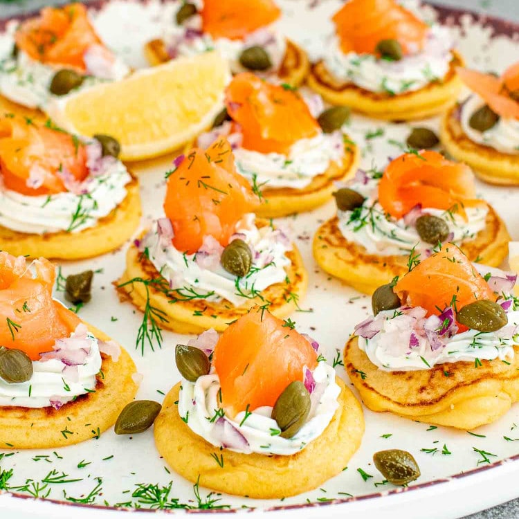 freshly made smoked salmon blinis on a white plate garnished with lemon wedges.