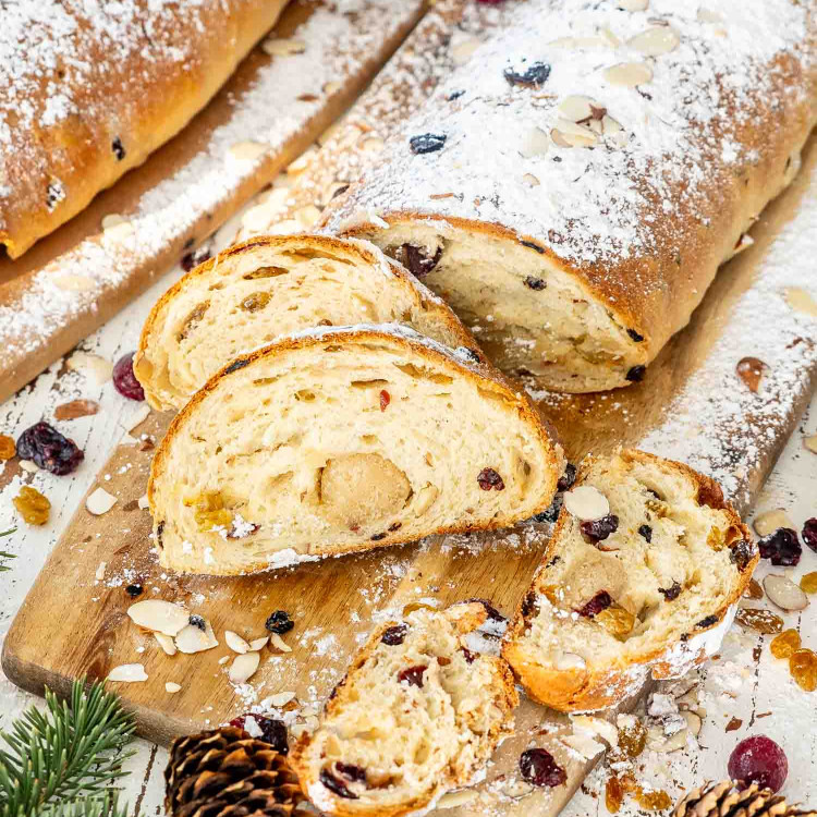 a cut up stollen dusted with powdered sugar on a cutting board.