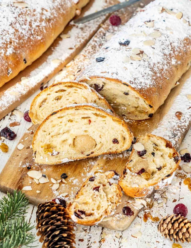 a cut up stollen dusted with powdered sugar on a cutting board.