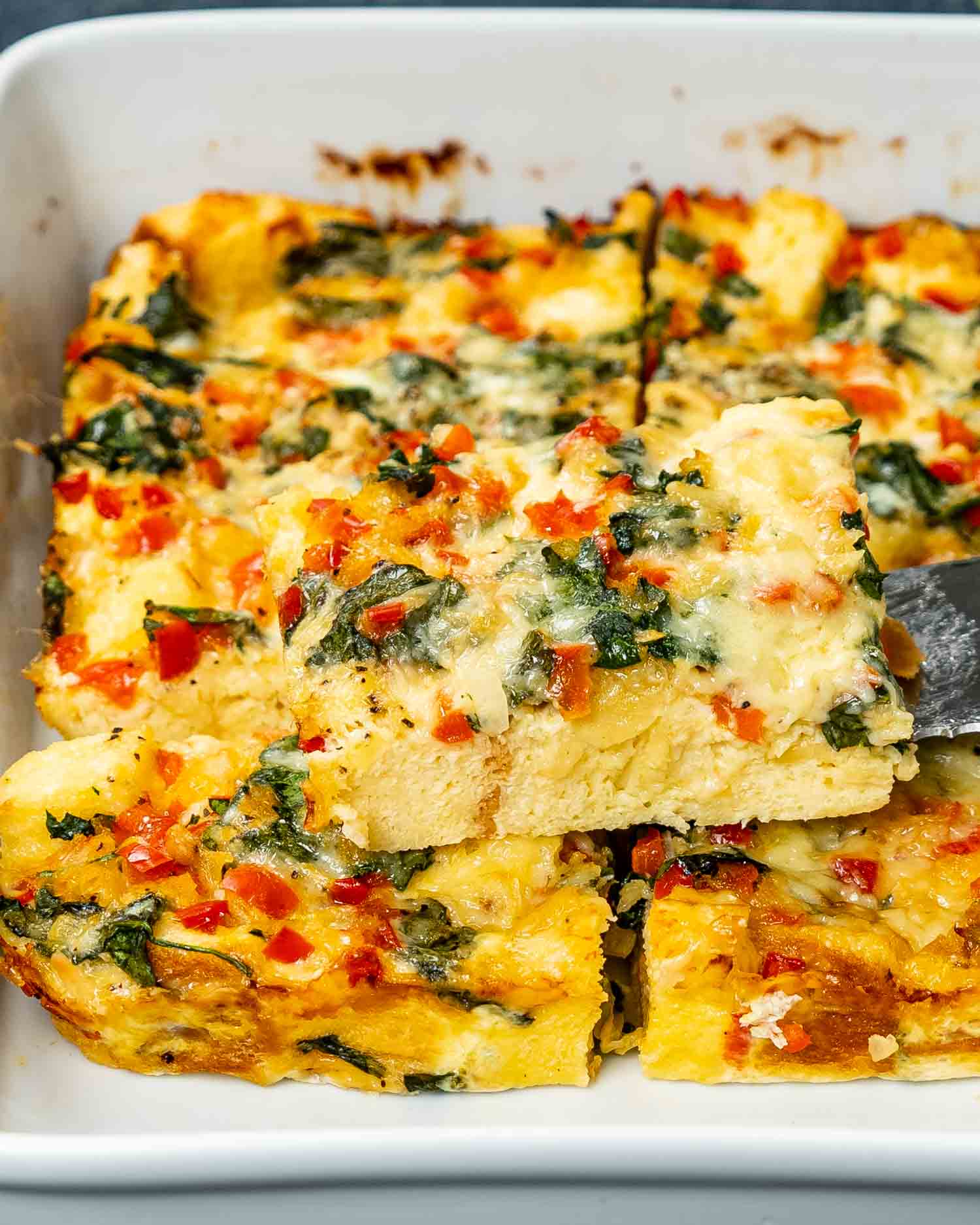 freshly baked strata cut into pieces in a white casserole dish.