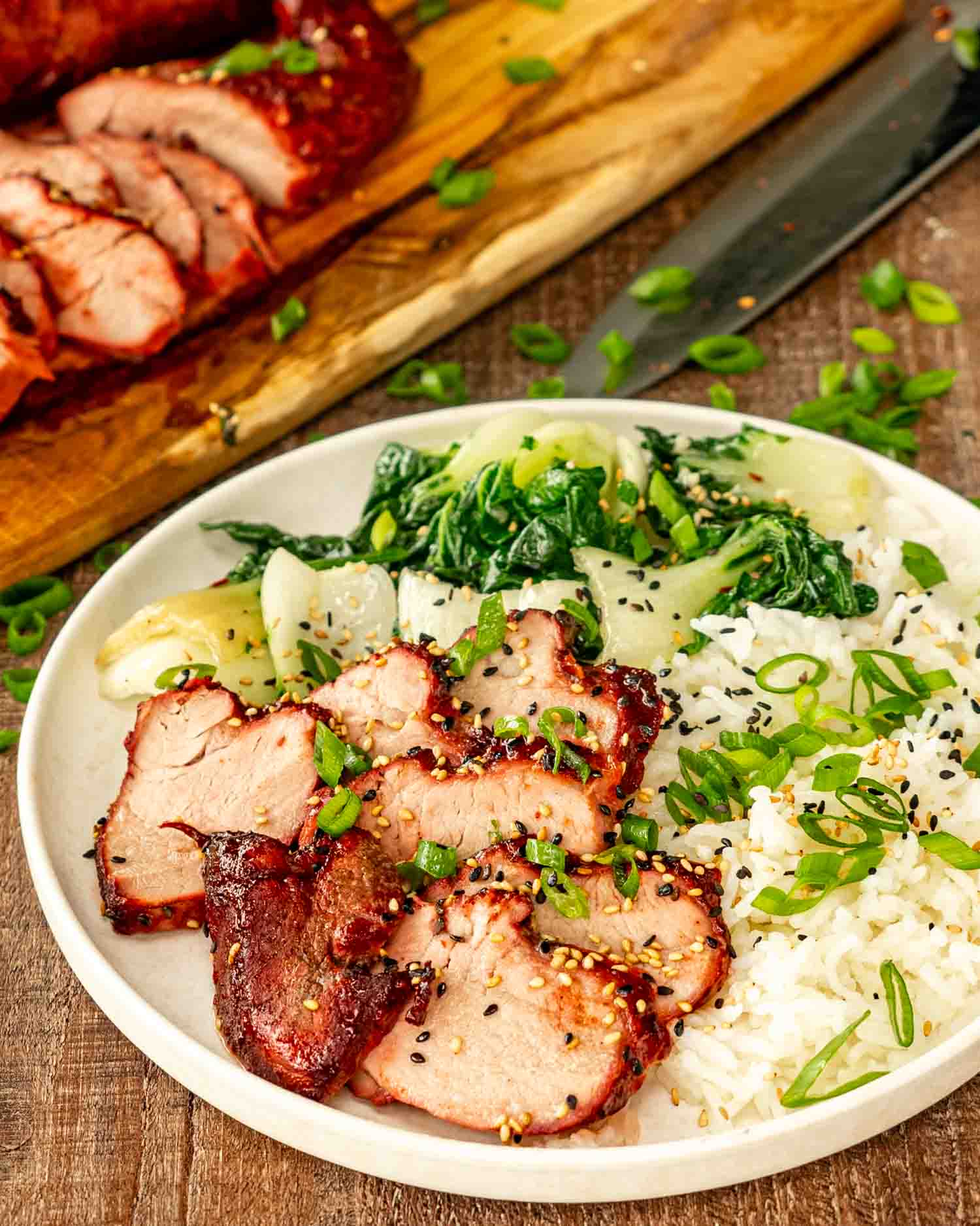 a few slices of char siu pork on a white plate with steamed rice and steamed broccoli.