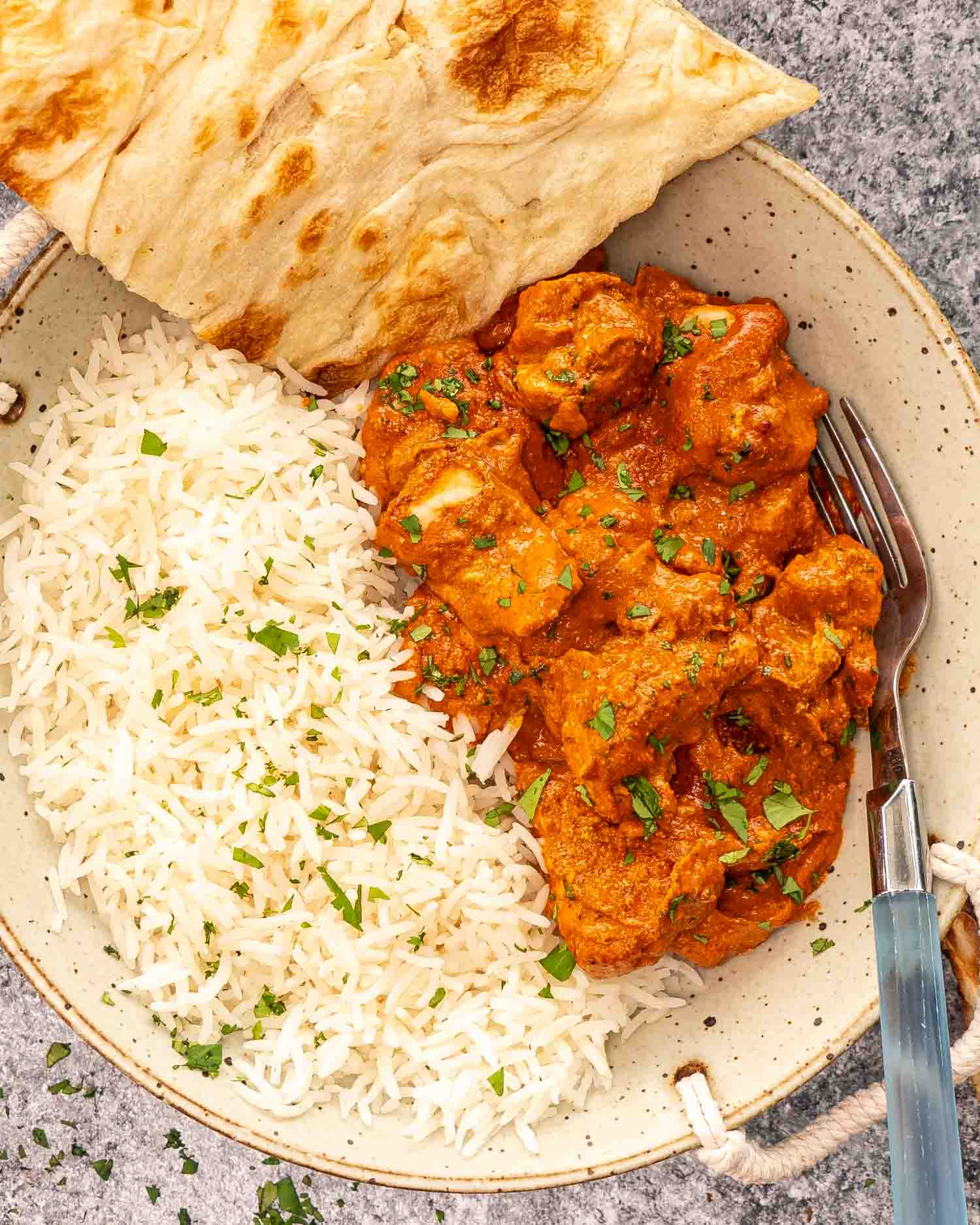 a serving of chicken tikka masala with rice and naan in a plate.